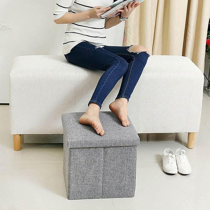 Grey foldable fabric storage stool with cushioned top for foot rest
