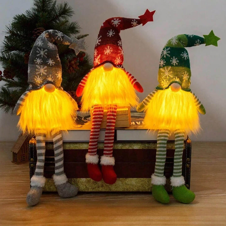 Three illuminated gnomes with colorful hats and striped pants sitting on a wooden box.