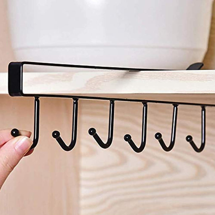 Black metal hook rack attached to a wooden shelf with a hand holding it.