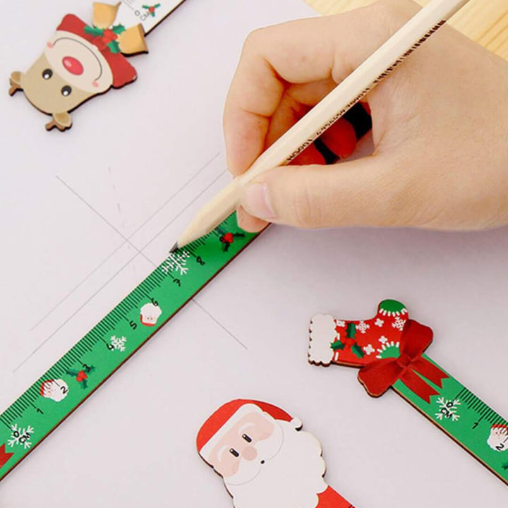 Hand holding a pencil near a Christmas-themed ruler with Santa, deer and stocking designs